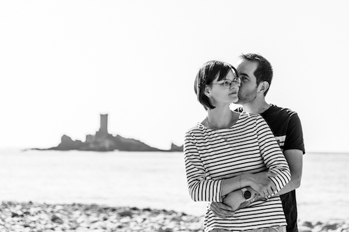 Photo en noir et blanc d'un couple sur la plage. Monsieur embrasse Madame dans le cou. 