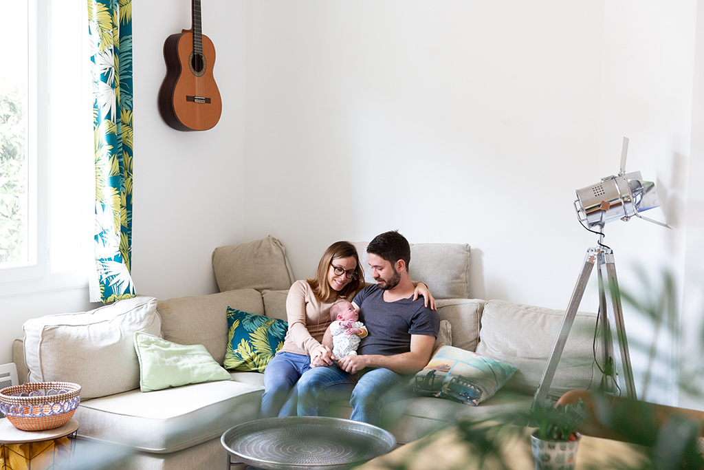 Un couple pose assis sur son canapé avec leur bébé lors d'une séance photo naissance à Tourrette Levens