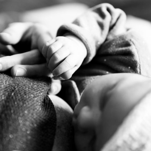 photo en noir et blanc d'un bébé tenant le doigt de sa maman. Myriam Ohayon Photographe naissance à Valbonne