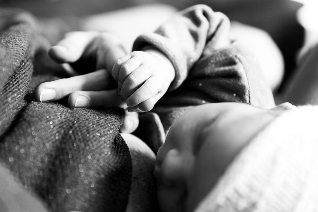 photo en noir et blanc d'un bébé tenant le doigt de sa maman. Myriam Ohayon Photographe naissance à Valbonne