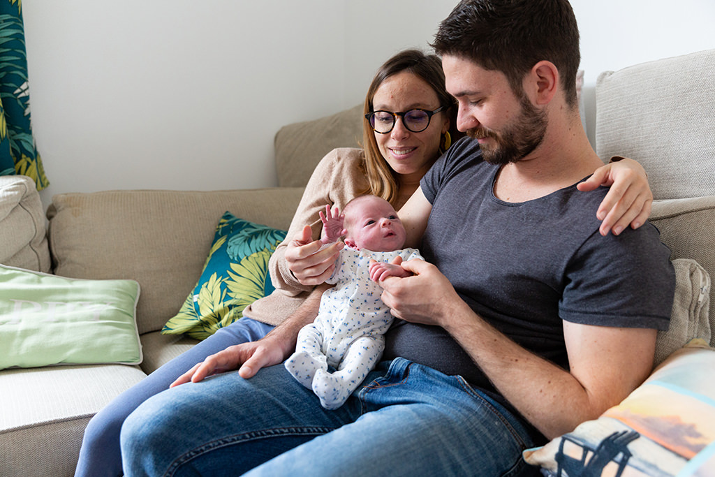 Un couple pose assis sur son canapé avec leur bébé lors d'une séance photo naissance à Tourrette Levens