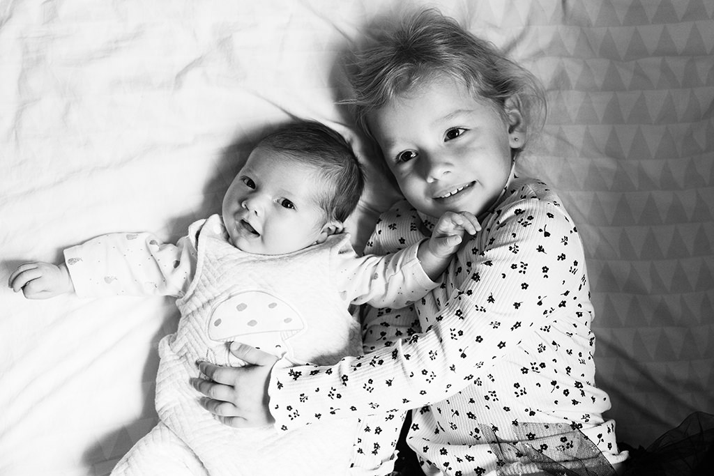 Un nouveau-né et sa grande soeur posent sur le lit lors d'une séance photo à Nice.