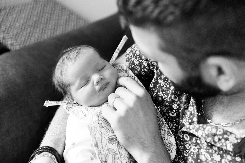 Photographie en noir et blanc d'un bébé dans les bras de son père. Séance photo naissance à Nice.