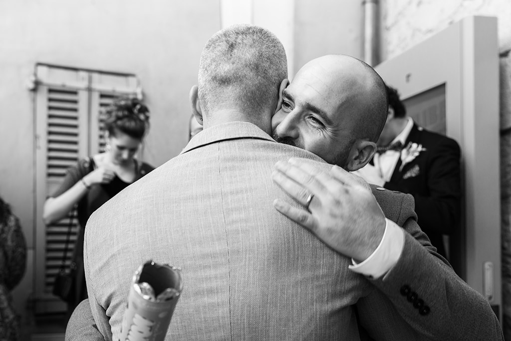 Un marié se fait féliciter par un ami à la sortie de la mairie de Fayence. Myriam Ohayon Photographe.