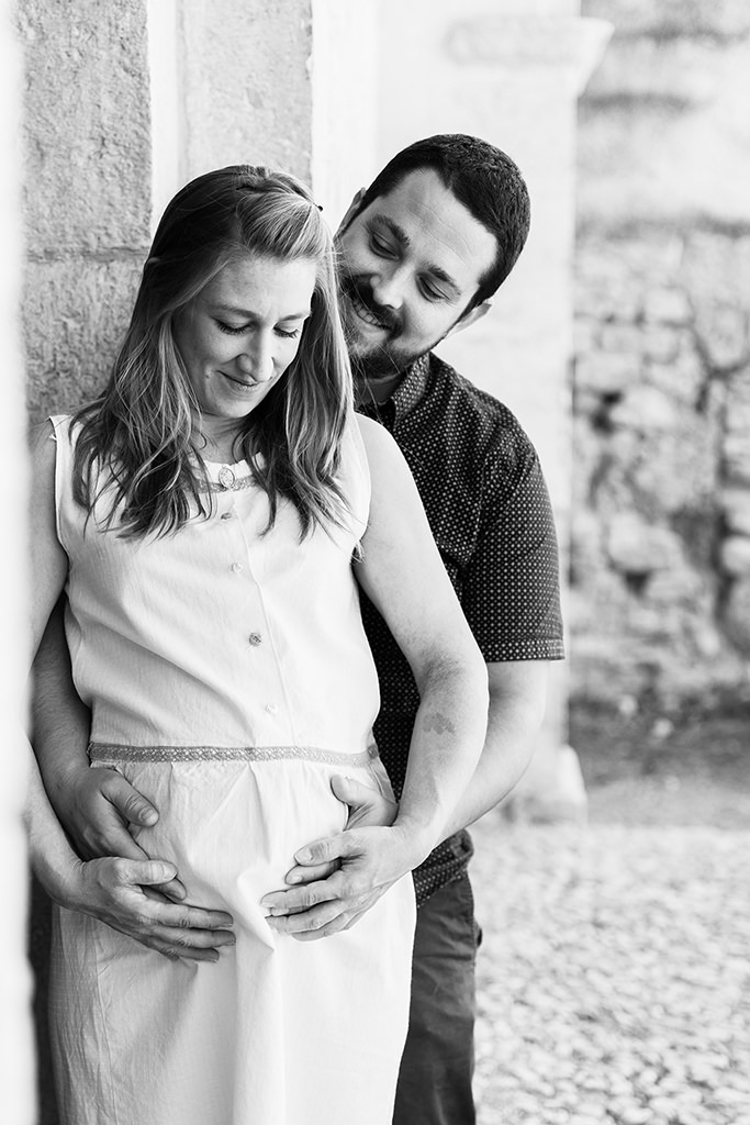 Photo en noir et blanc d'une femme enceinte et de son mari qui l'enlace tendrement lors d'une séance photo grossesse à Seillans.