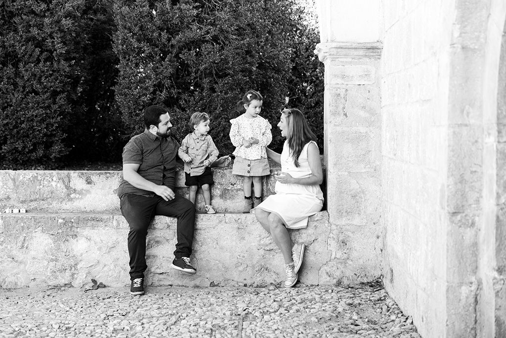 Photo en noir et blanc prise sur le vif d'une famille avec la maman, le papa et les deux jeunes enfants. Ils discutent entre eux lors d'une séance photo grossesse. Myriam Ohayon Photographe