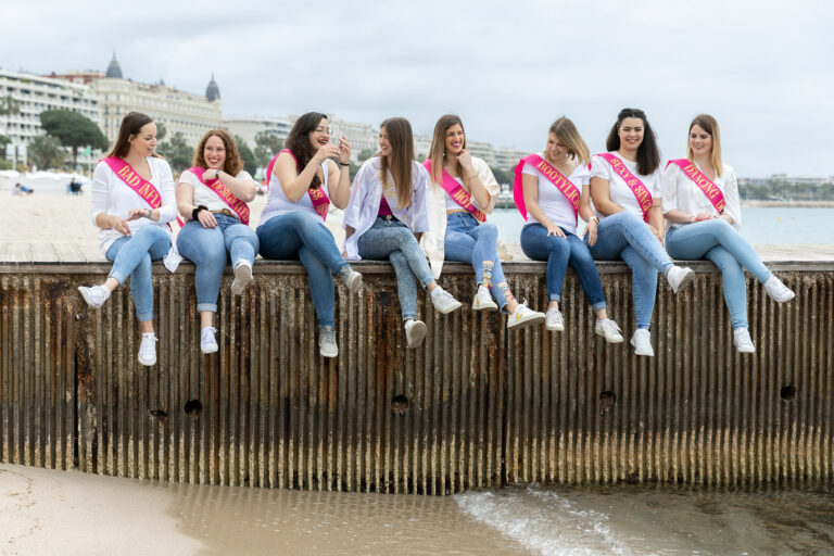 Séance photo EVJF à Cannes : des amies rient assises sur un ponton de la plage de la Croisette.
