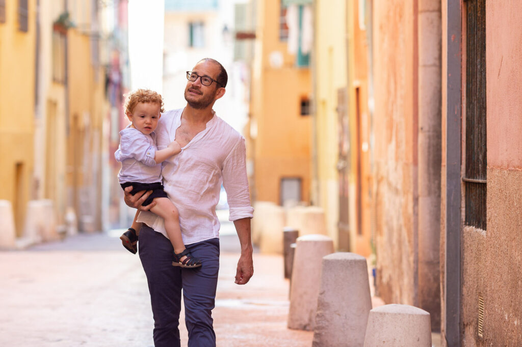 Séance photo lifestyle en famille à Nice. Photo d'un père et son fils de deux ans dans ses bras prise en lumière naturelle dans le Vieux-Nice.