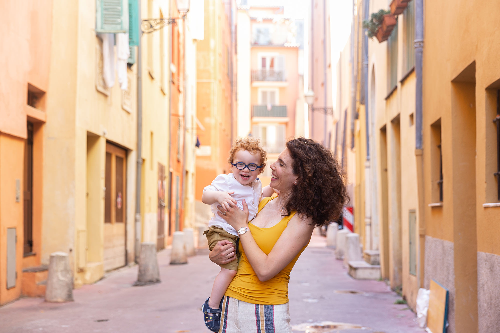Séance photo lifestyle en famille à Nice. Photo d'une mère et son fils de deux ans riant dans ses bras prise en lumière naturelle dans le Vieux-Nice.