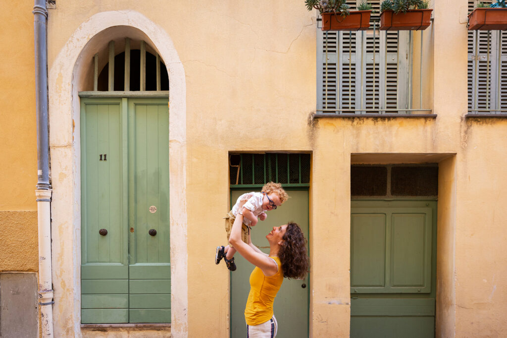 Séance photo lifestyle en famille à Nice. Photo d'une mère et son fils de deux ans riant dans ses bras prise en lumière naturelle dans le Vieux-Nice.