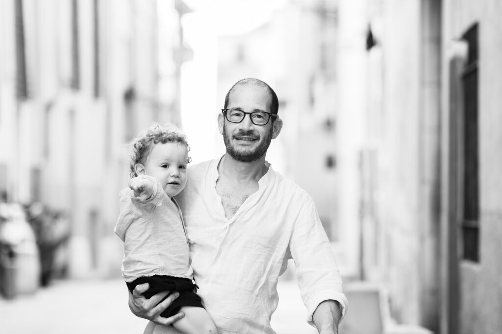 Séance photo lifestyle en famille à Nice. Photo en noir et blanc d'un père et son fils de deux ans dans ses bras prise en lumière naturelle dans le Vieux-Nice.