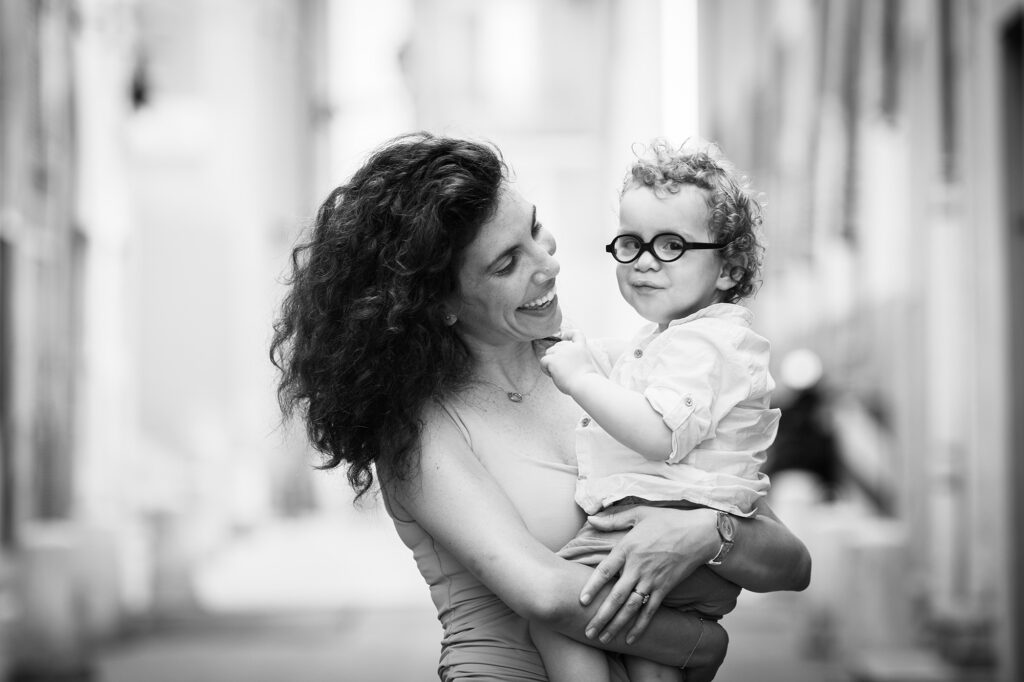 Séance photo lifestyle en famille à Nice. Photo en noir et blanc d'une mère et son fils de deux ans dans ses bras prise en lumière naturelle dans le Vieux-Nice.